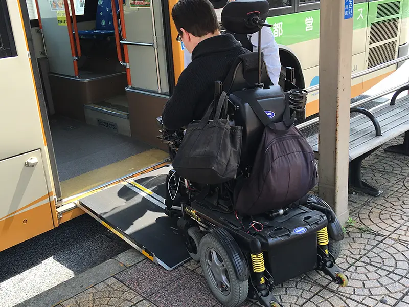 A person using a power wheelchair boarding a bus in Japan via a portable ramp